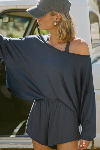 Front view of model posing next to a truck in the full-length navy modal Relaxed Long Sleeve top with dropped shoulders and a wide neckline that can be worn off the shoulders.