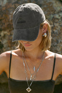 Front view of model posing outside wearing the six-panel washed black Official Cap with a curved brim and an embroidered upside down Joah Brown logo on the front