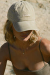 Front view of model posing outside wearing the six-panel desert Official Cap with a curved brim and an embroidered upside down Joah Brown logo on the front