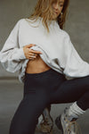 Front view of model kneeling on the ground posing in the comfortable sahara french terry Turtleneck Sweatshirt pullover with a side split in the collar and a slightly oversized fit