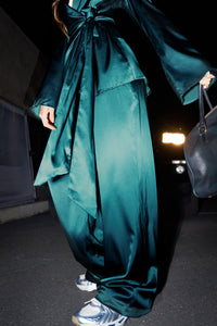 Close up front view of model from the bust down posing outside in front of a car in the soft and smooth classic pleated lagoon silk Relaxed Silk Trouser with a flattering wide leg, zip fly and side pockets.