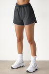 Front view of model from the waist down posing in the relaxed fit washed black french terry Sweat Short with side pockets, hidden drawstring, and an adjustable elastic waistband.