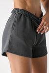 Close up side view of model from the waist down posing in the relaxed fit washed black french terry Sweat Short with side pockets, hidden drawstring, and an adjustable elastic waistband.