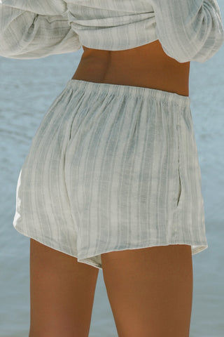 Close up back view of model from the waist down posing in the relaxed fit lightweight natural white and blue stripe gauze Relaxed Everyday Short with an elastic waistband and adjustable front tie