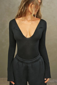 Front view of model posing in the fitted black modal Notched V Neck Long Sleeve top with a deep notched V-neckline, extra long sleeves and small side slits at the hem