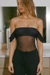Front view of model posing in the sheer and fitted black mesh Off The Shoulder Bandeau Tank with thin straps and draped sleeves and can be worn off the shoulder or with the sleeves up