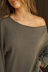 Close up detail front view of model posing in the relaxed fit army luxe knit Off Shoulder Tunic with a wide off-the-shoulder neckline and asymmetrical hem