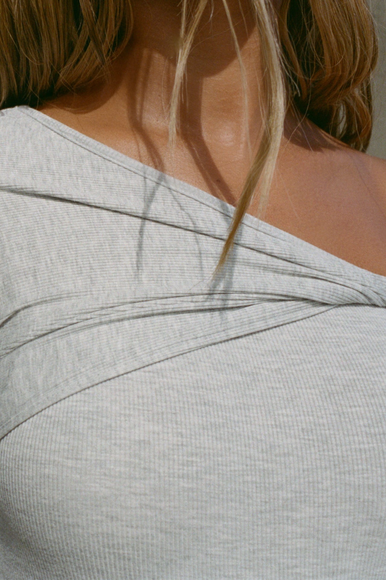 Close up detail front view of model posing in the fitted pearl grey rib Off Shoulder Twist Long Sleeve top asymmetrical neckline with a twist detail and off-shoulder design