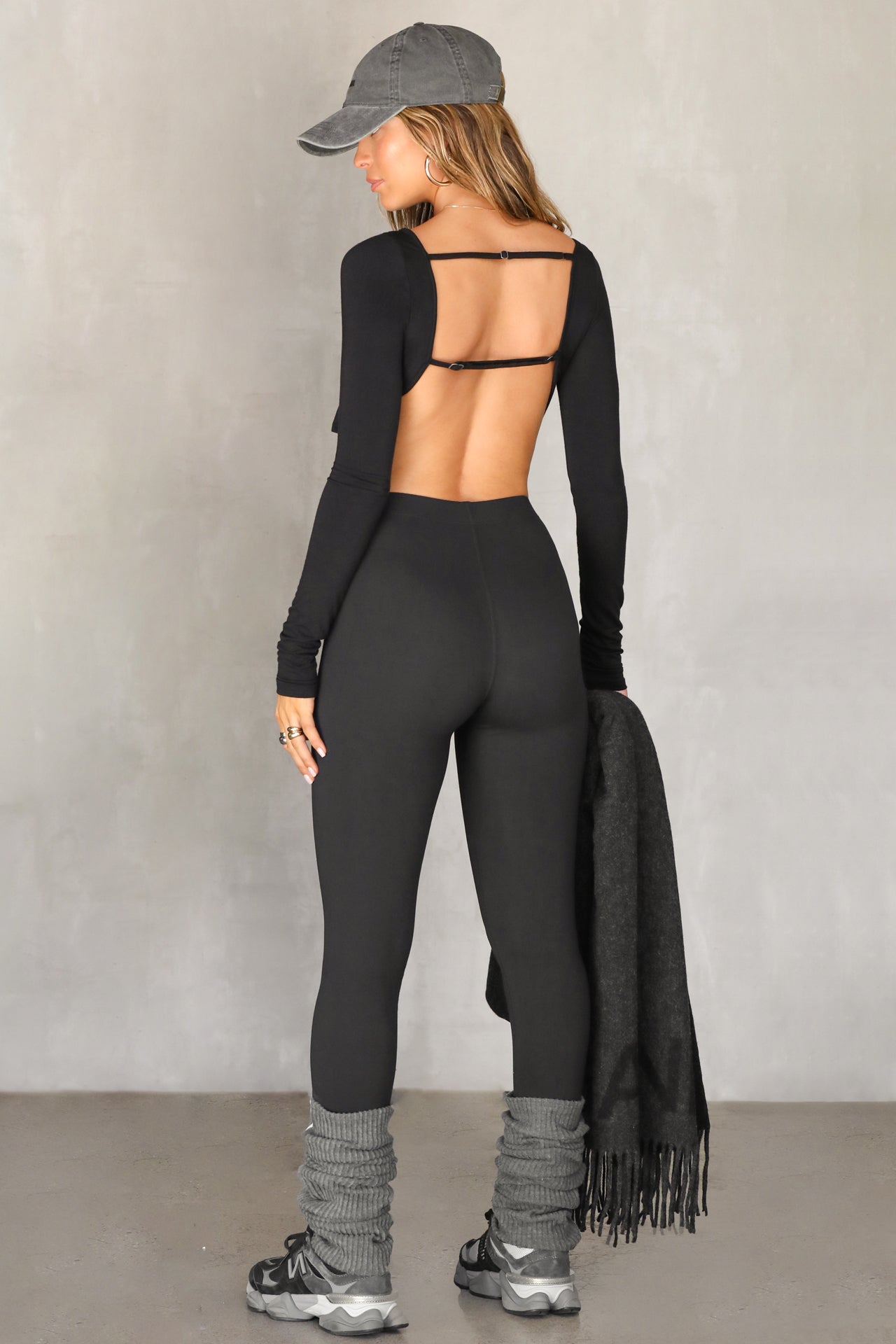 Full body back view of model posing in the fitted and cropped black modal Open Boatneck Long Sleeve top with a high neckline,curved hem, open back and adjustable strap details