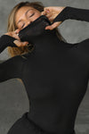 Front view of model posing in the fitted black modal Open Back Turtleneck long sleeve top with thumbholes at the bottom of the sleeves