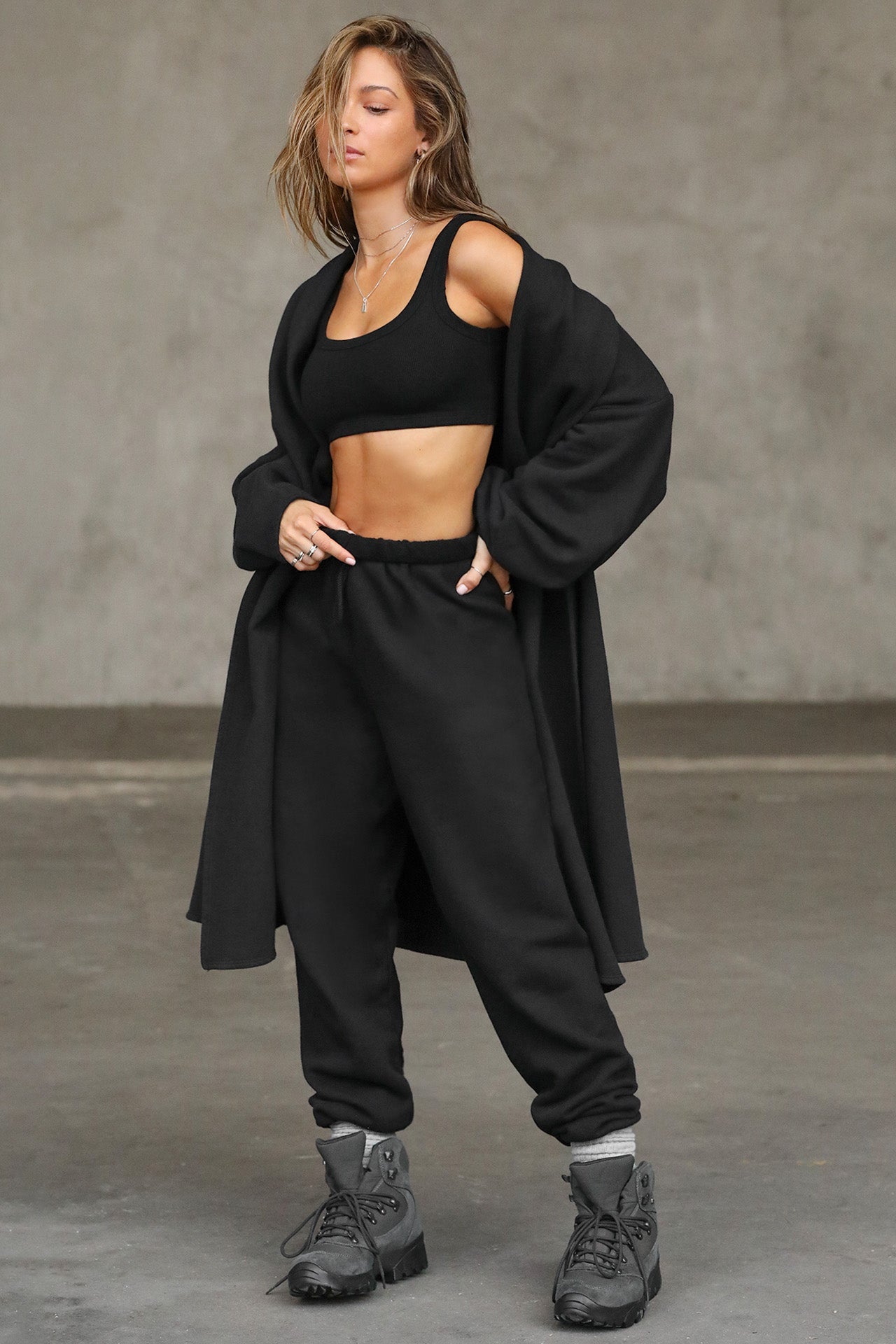 Full body front view of model posing in the knee-length loose fitting black french terry Oversized Cardigan with a rolled neckline and extra long sleeves