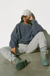 Front view of model sitting on the floor posing in the relaxed fit washed navy french terry Oversized Crew Pullover sweatshirt with dropped sleeves and a ribbed crew neckline