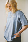 Side view of model posing in the relaxed fit denim cotton Oversized Crew Tee with a crew neckline and joah brown logo patch on the upper left side