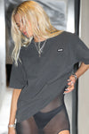 Front view of model posing in the relaxed fit washed black cotton Oversized Crew Tee with a crew neckline and joah brown logo patch on the upper left side