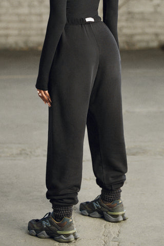 Back view of model from the waist down wearing the oversized loose fit black french terry Oversized Jogger with an elastic waistband and ankle cuffs