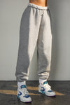 Side view of model from the waist down wearing the oversized loose fit classic grey french terry Oversized Jogger with an elastic waistband and ankle cuffs