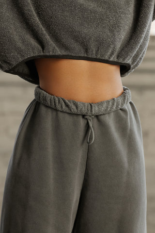 Close up detail front view of model from the waist down posing in the oversized loose fit washed black french terry Oversized Jogger with an elastic waistband and ankle cuffs