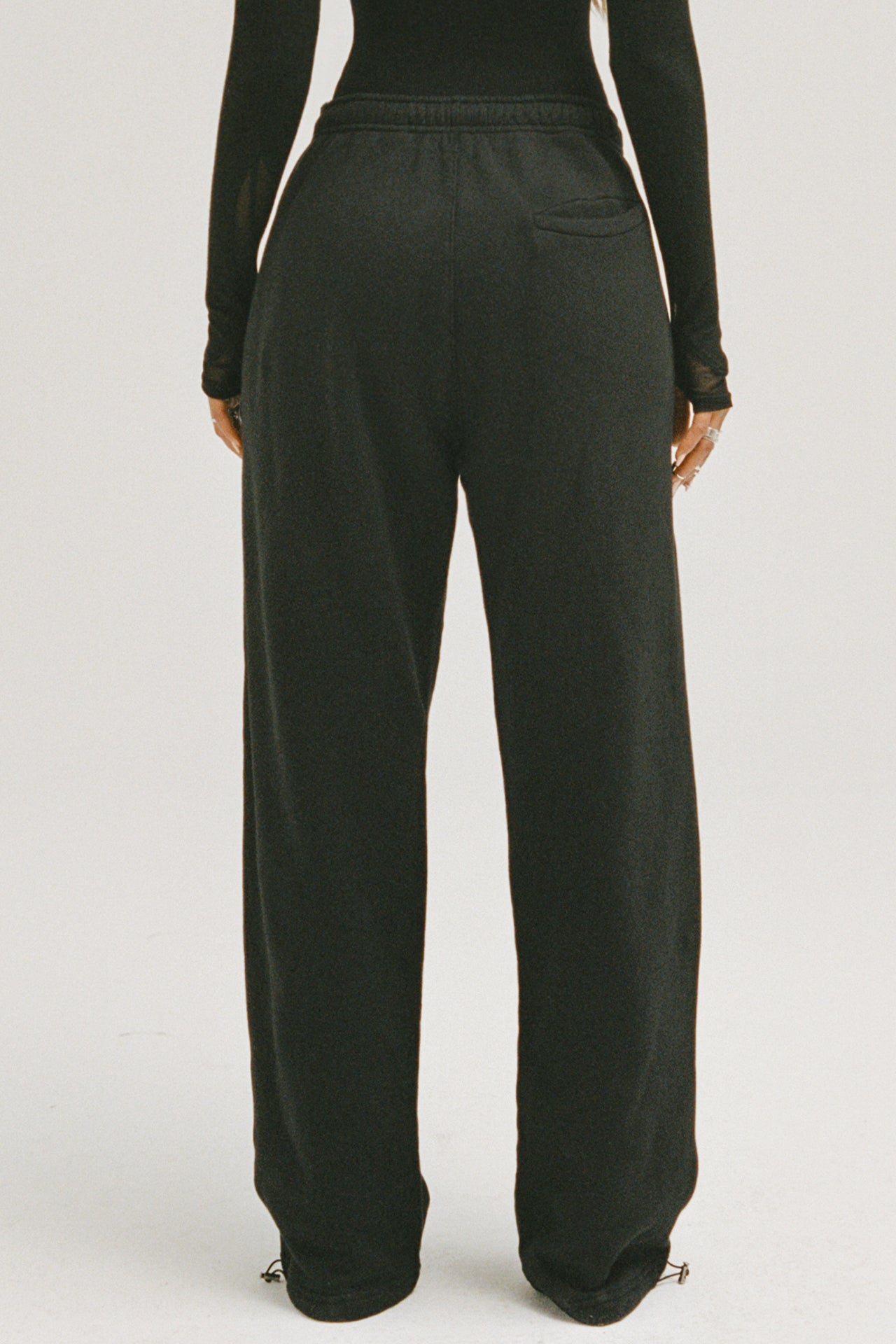 Front view of model from the waist down posing in the relaxed fit black french terry Oversized Straight Leg Jogger with an elastic waistband, hidden drawstring, pocket details. and adjustable cinching at the ankle cuffs