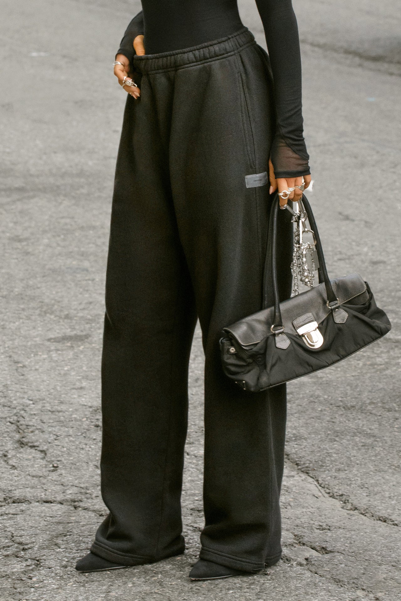 Side view of model from the waist down posing outside in the street in the relaxed fit black french terry Oversized Straight Leg Jogger with an elastic waistband, hidden drawstring, pocket details. and adjustable cinching at the ankle cuffs