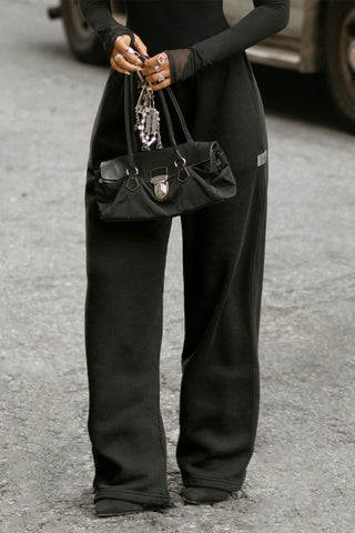 Front view of model from the waist down posing outside in the street in the relaxed fit black french terry Oversized Straight Leg Jogger with an elastic waistband, hidden drawstring, pocket details. and adjustable cinching at the ankle cuffs