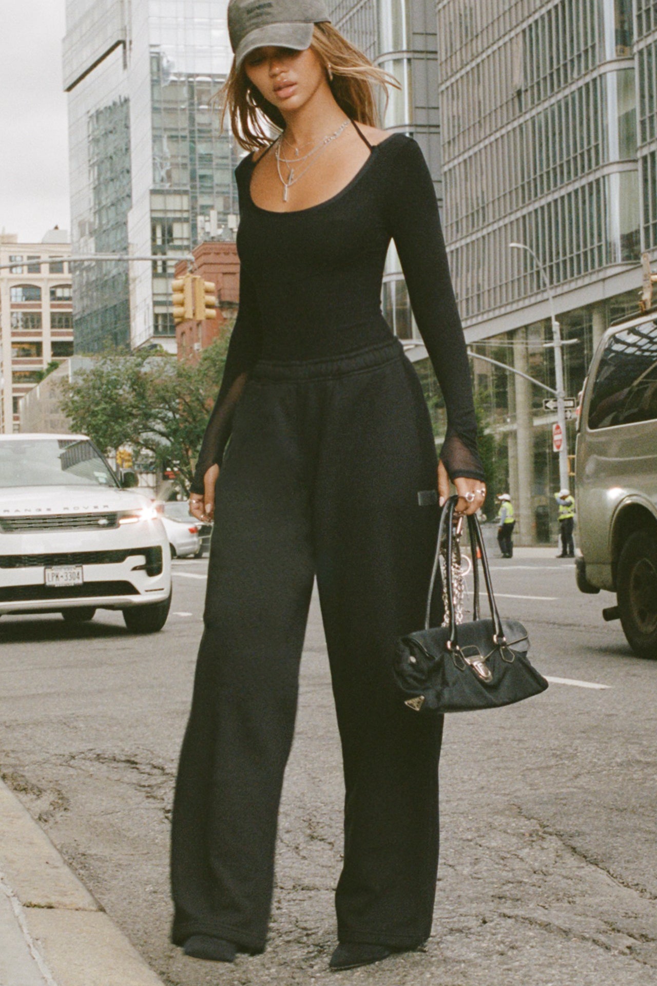 Full body front of model posing outside in the street in the relaxed fit black french terry Oversized Straight Leg Jogger with an elastic waistband, hidden drawstring, pocket details. and adjustable cinching at the ankle cuffs