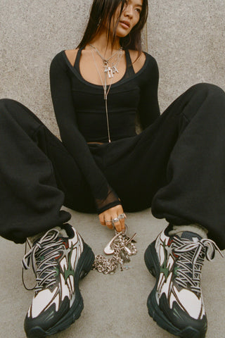 Front of model leaning against a wall outside in the  relaxed fit black french terry Oversized Straight Leg Jogger with an elastic waistband, hidden drawstring, pocket details. and adjustable cinching at the ankle cuffs
