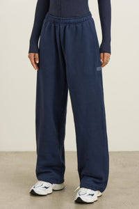 Front view of model from the waist down posing in the relaxed fit midnight navy french terry Oversized Straight Leg Jogger with an elastic waistband, hidden drawstring, pocket details. and adjustable cinching at the ankle cuffs