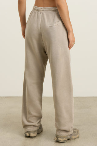 Back view of model from the waist down posing in the relaxed fit sand french terry Oversized Straight Leg Jogger with an elastic waistband, hidden drawstring, pocket details. and adjustable cinching at the ankle cuffs