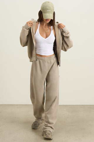 Full body front view of model posing in the relaxed fit sand french terry Oversized Straight Leg Jogger with an elastic waistband, hidden drawstring, pocket details. and adjustable cinching at the ankle cuffs