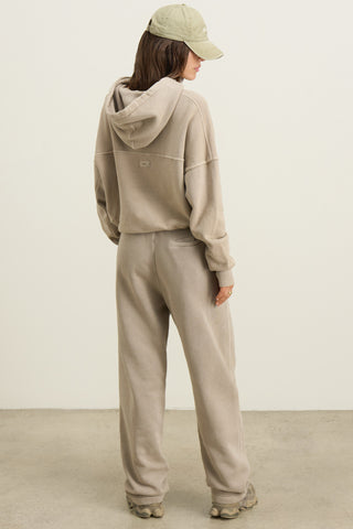 Full body back view of model posing in the relaxed fit sand french terry Oversized Straight Leg Jogger with an elastic waistband, hidden drawstring, pocket details. and adjustable cinching at the ankle cuffs