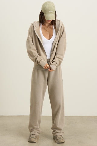 Full body front view of model posing in the relaxed fit sand french terry Oversized Straight Leg Jogger with an elastic waistband, hidden drawstring, pocket details. and adjustable cinching at the ankle cuffs