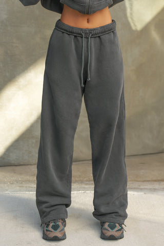 Front view of model from the waist down posing in the relaxed fit washed black french terry Oversized Straight Leg Jogger with an elastic waistband, hidden drawstring, pocket details. and adjustable cinching at the ankle cuffs