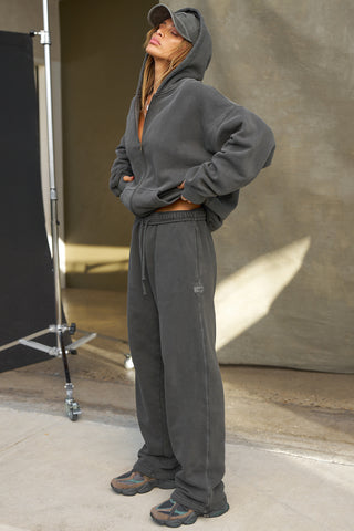 Full body side view of model posing in the relaxed fit washed black french terry Oversized Straight Leg Jogger with an elastic waistband, hidden drawstring, pocket details,  adjustable cinching at the ankle cuffs and a custom Joah Brown logo patch below the pocket