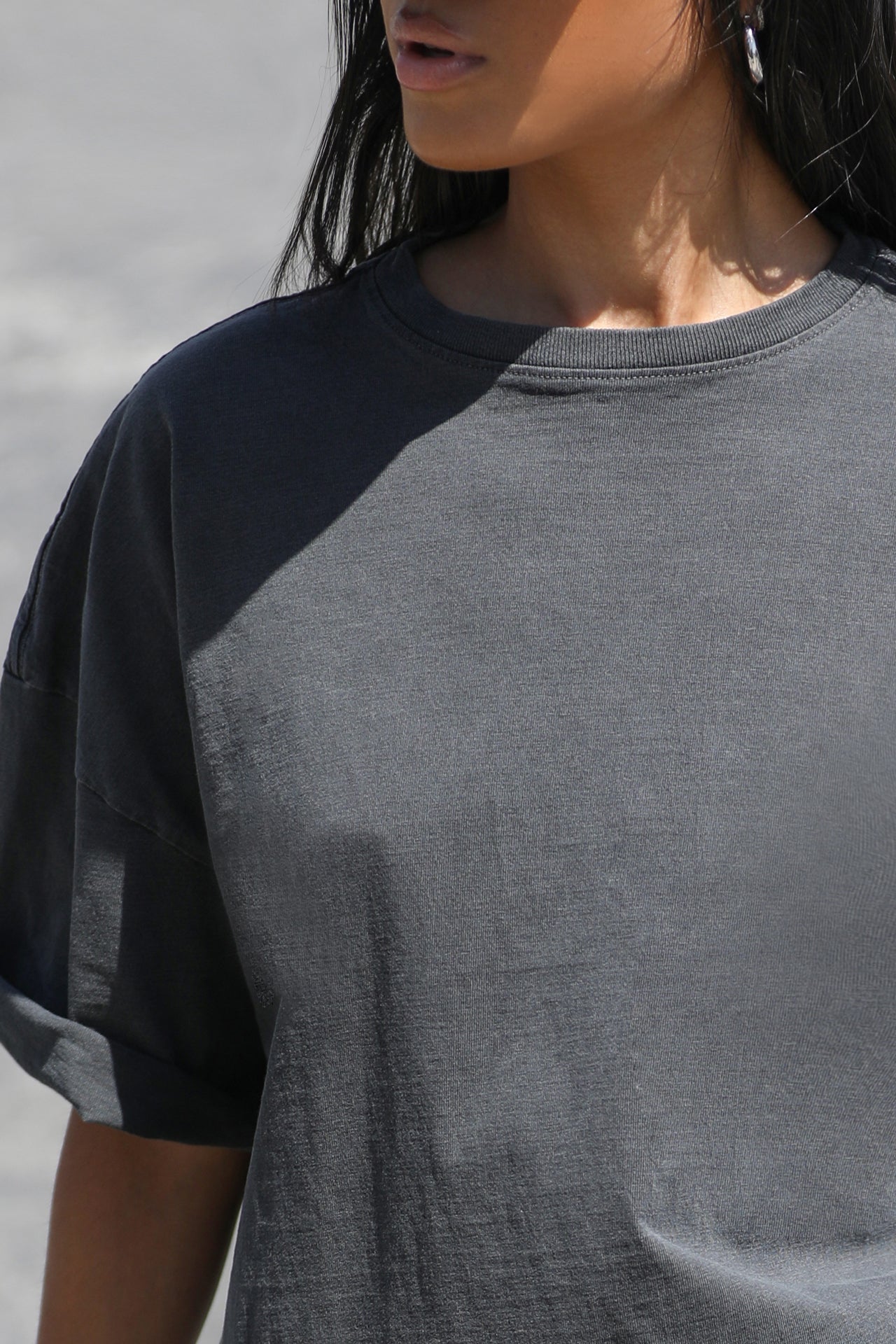 Close up detail front view of model posing the relaxed fit washed black cotton Oversized Vintage Tee with dropped shoulders and a crew neckline
