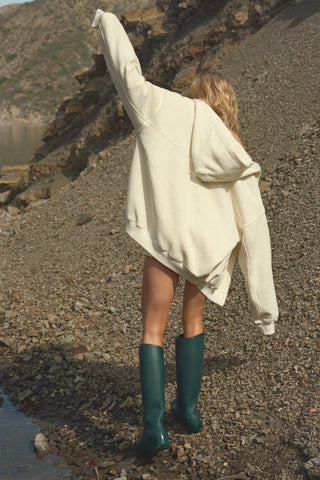 Back view of model posing outside in the relaxed fit buttercream french terry Classic Zip Hoodie with a full length front zip closure, side pockets and thumbholes in the fitted cuffs