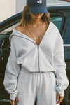 Front view of model posing in the oversized comfortable pearl grey french terry Oversized Zip Hoodie with a full length front zip closure, side pockets and thumbholes in the fitted cuffs