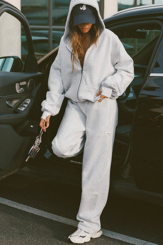 Front view of model standing next to a car posing in the oversized comfortable pearl grey french terry Oversized Zip Hoodie with a full length front zip closure, side pockets and thumbholes in the fitted cuffs
