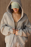 Front view of model posing in the oversized comfortable sand french terry Empire Zip Hoodie with a full length front zip closure, side pockets and thumbholes in the fitted cuffs