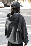 Back view of model posing in the oversized comfortable washed black french terry Oversized Zip Hoodie with a full length front zip closure, side pockets and thumbholes in the fitted cuffs