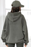 Back view of model posing in the oversized comfortable washed sage french terry Oversized Zip Hoodie with a full length front zip closure, side pockets and thumbholes in the fitted cuffs