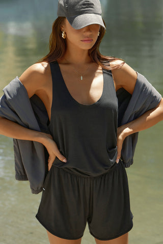 Front view of model posing outside by a lake in the lightweight relaxed fit black modal Plunge Tank with a plunging u-neckline