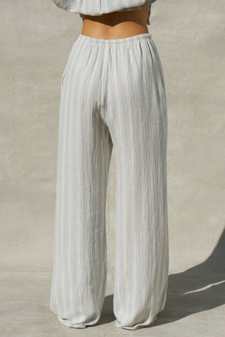Back view of model from the waist down posing in the relaxed fit lightweight natural white and blue stripe gauze Relaxed Everyday Pant with an elastic waistband and adjustable front tie