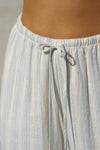 Close up detail front view of model from the waist down posing in the relaxed fit lightweight natural white and blue stripe gauze Relaxed Everyday Pant with an elastic waistband and adjustable front tie