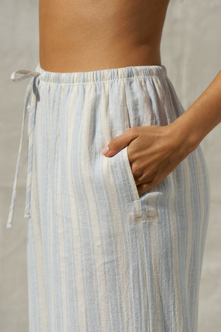 Close up side view of model from the waist down posing in the relaxed fit lightweight natural white and blue stripe gauze Relaxed Everyday Pant with an elastic waistband and adjustable front tie
