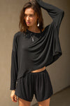Front view of model posing in the full-length black modal Relaxed Long Sleeve top with dropped shoulders and a wide neckline that can be worn off the shoulders.