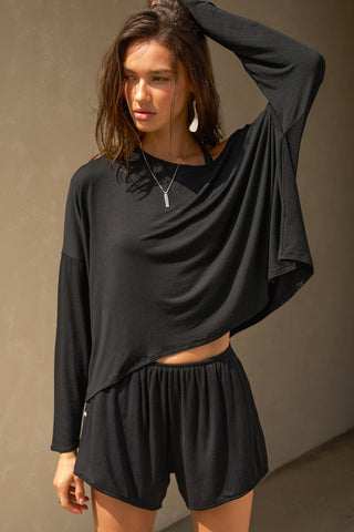 Front view of model posing in the full-length black modal Relaxed Long Sleeve top with dropped shoulders and a wide neckline that can be worn off the shoulders.