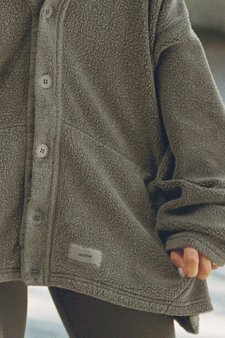 Close up front detail view of model posing in the loose-fitting oakmoss sherpa Relaxed Shirt Jacket with a classic collar, front button closures, side pockets, and a curved hem.