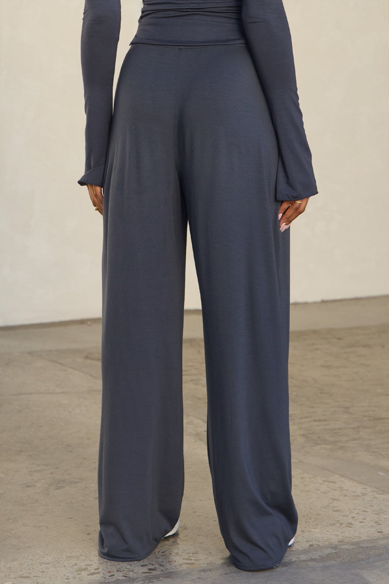 Back view of model from the waist down posing in the relaxed fit navy modal Relaxed Straight Leg Pant with a wide leg, elastic waistband, adjustable drawstring tie and subtle pleating at the sides.