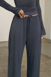 Front view of model from the waist down posing in the relaxed fit navy modal Relaxed Straight Leg Pant with a wide leg, elastic waistband, adjustable drawstring tie and subtle pleating at the sides.