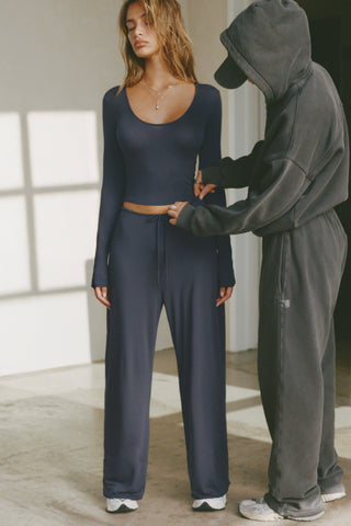 Full body front view of model posing in the relaxed fit navy modal Essential Straight Leg Pant with a wide leg, elastic waistband, adjustable drawstring tie and subtle pleating at the sides.